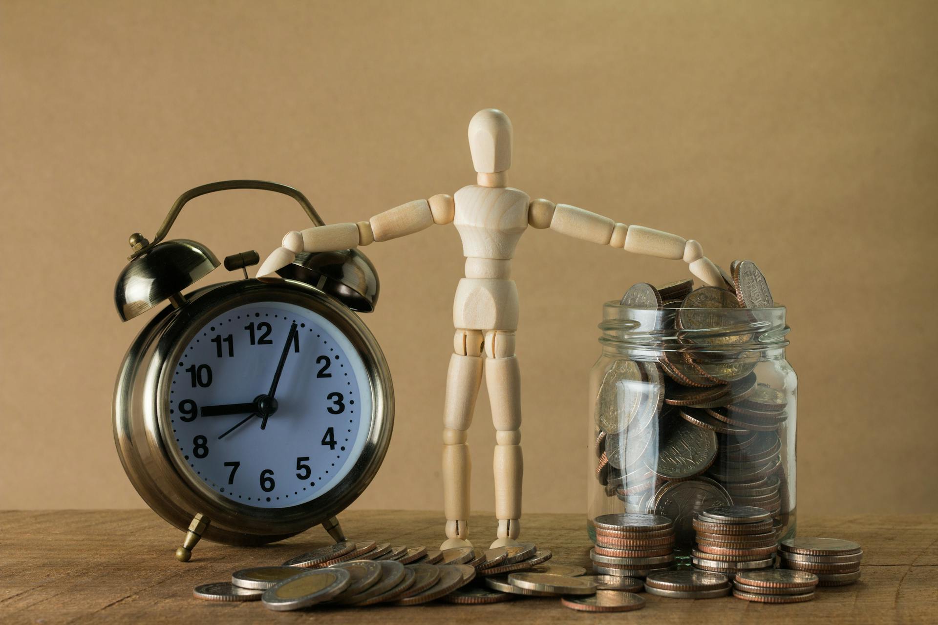 A wooden toy in between a jar of coins and an alarm clock | Source: Pexels