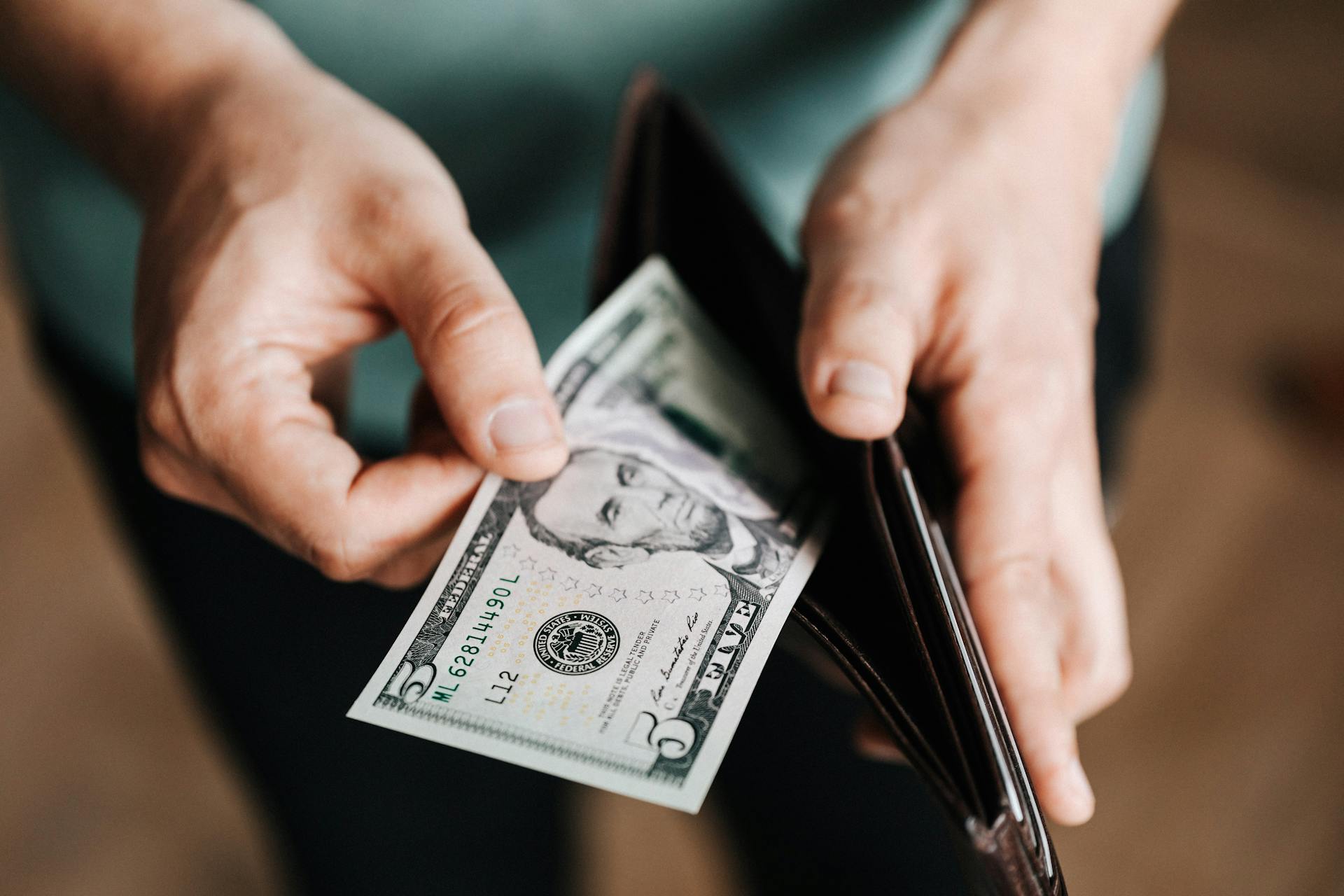 A closeup of a person pulling out a $5 bill from their wallet | Source: Pexels