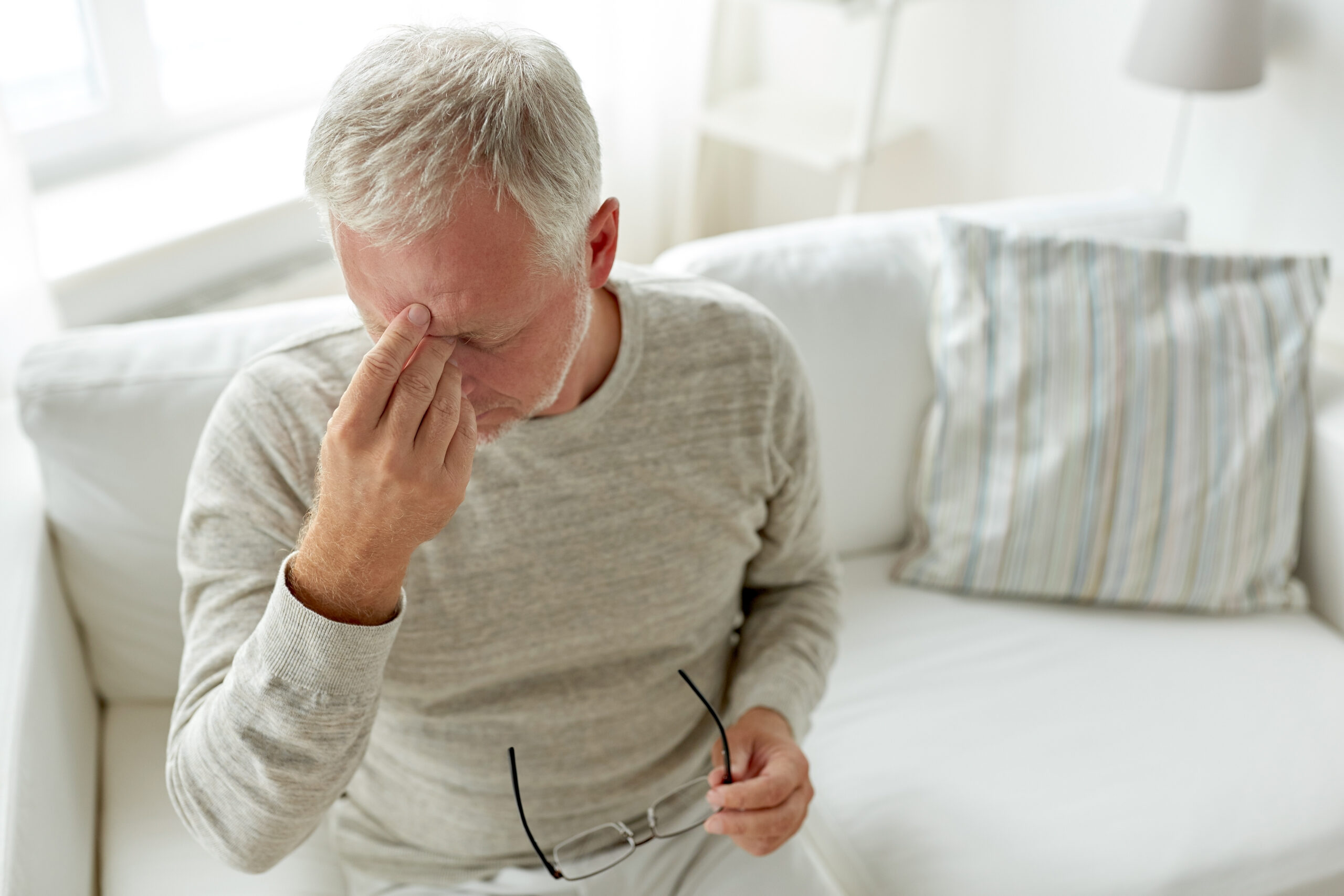 A stressed old man holding his glasses in one hand while pressing his fingers against the top of his nose | Source: Shutterstock