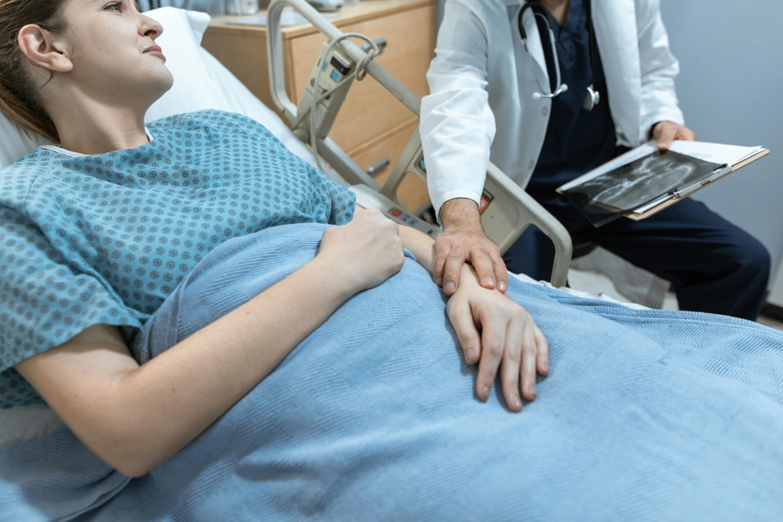 A woman being comforted by a doctor while lying in a hospital bed | Source: Pexels