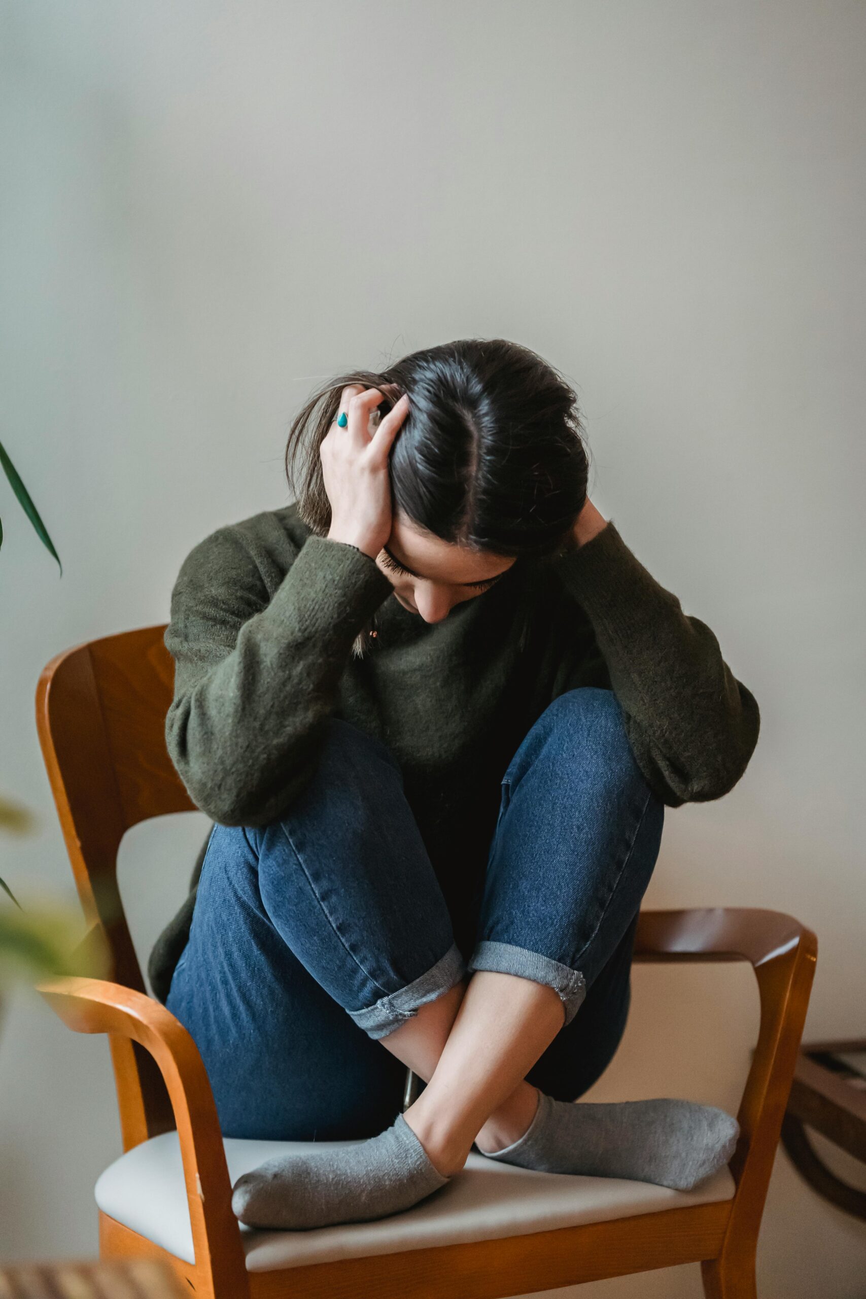 A distressed woman sitting with her head down, hands over her ears, and legs crossed | Source: Pexels