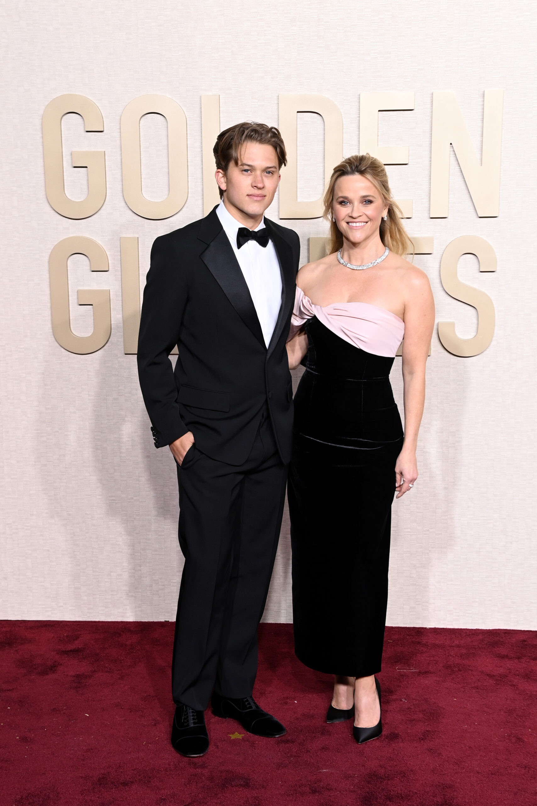 Deacon Phillippe and Reese Witherspoon pose on the red carpet at the 81st Annual Golden Globe Awards, with him in a tuxedo and her in a black-and-pink gown.