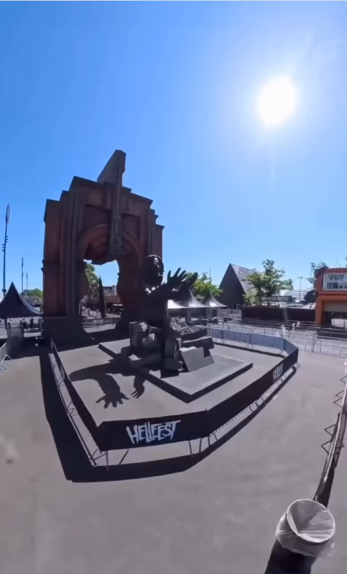 Ozzy Osbourne's "Prince of Darkness" statue is displayed at Hellfest in Clisson, France, beneath a towering archway featuring the festival's emblem. The monument sits on a raised platform under clear skies ahead of its official unveiling.
