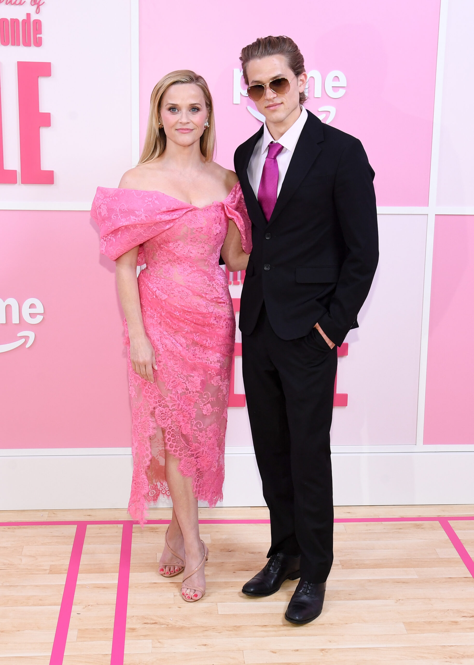 Reese Witherspoon and Deacon Phillippe pose at Prime Video's "Elle" New York premiere, coordinated against the pink backdrop as he wears a black suit and magenta tie.
