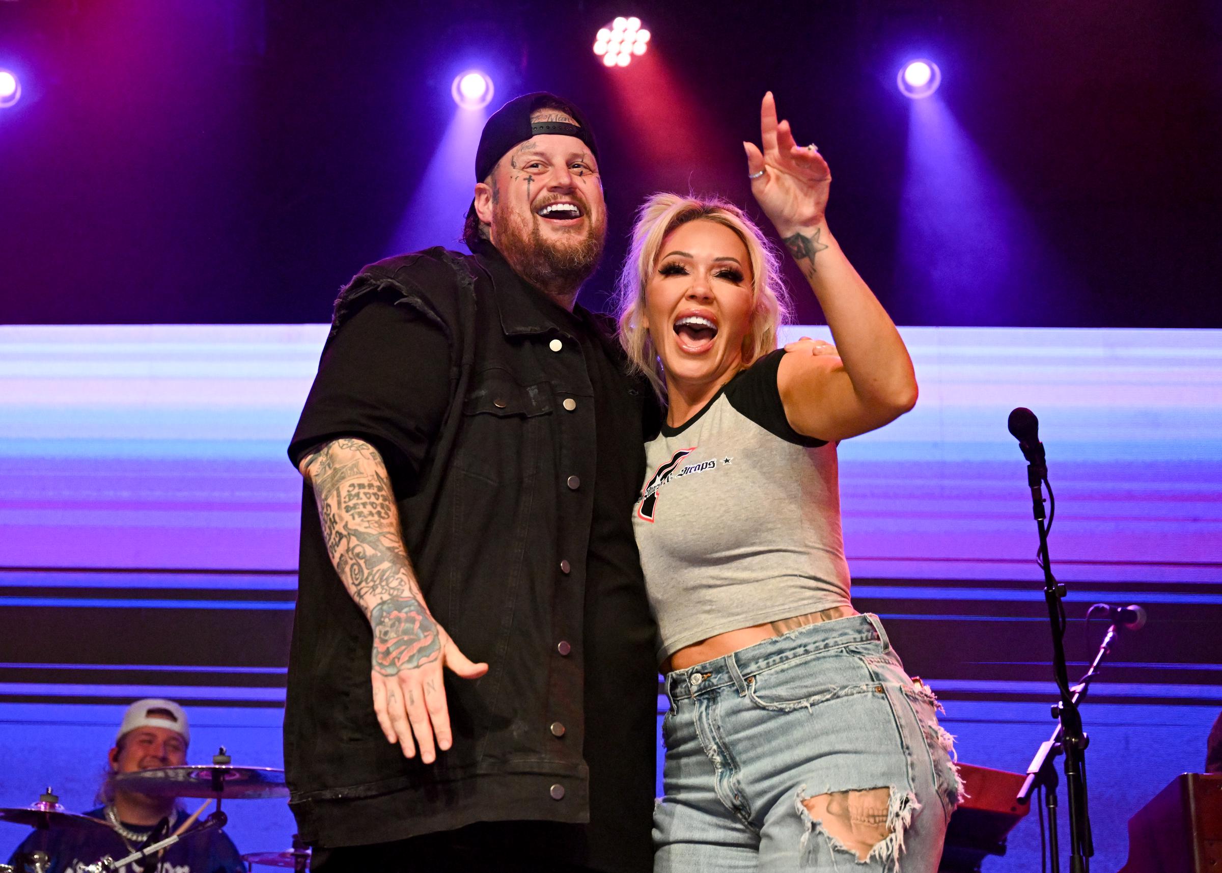 Jelly Roll and Bunnie XO smile and embrace onstage during a live performance, appearing in high spirits under colorful stage lights. The photo resurfaced as a source claimed the former couple, who are divorcing after nearly a decade of marriage, "still love each other."