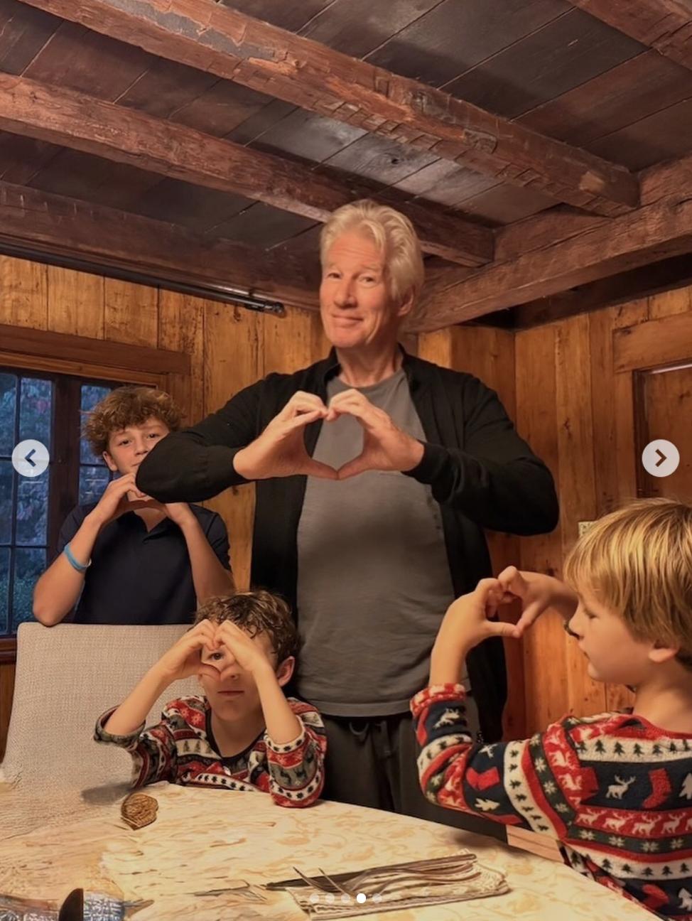 Richard Gere and his children gather around a dining table inside the family's Spain home, where exposed wooden beams and paneled walls create a warm, rustic atmosphere.
