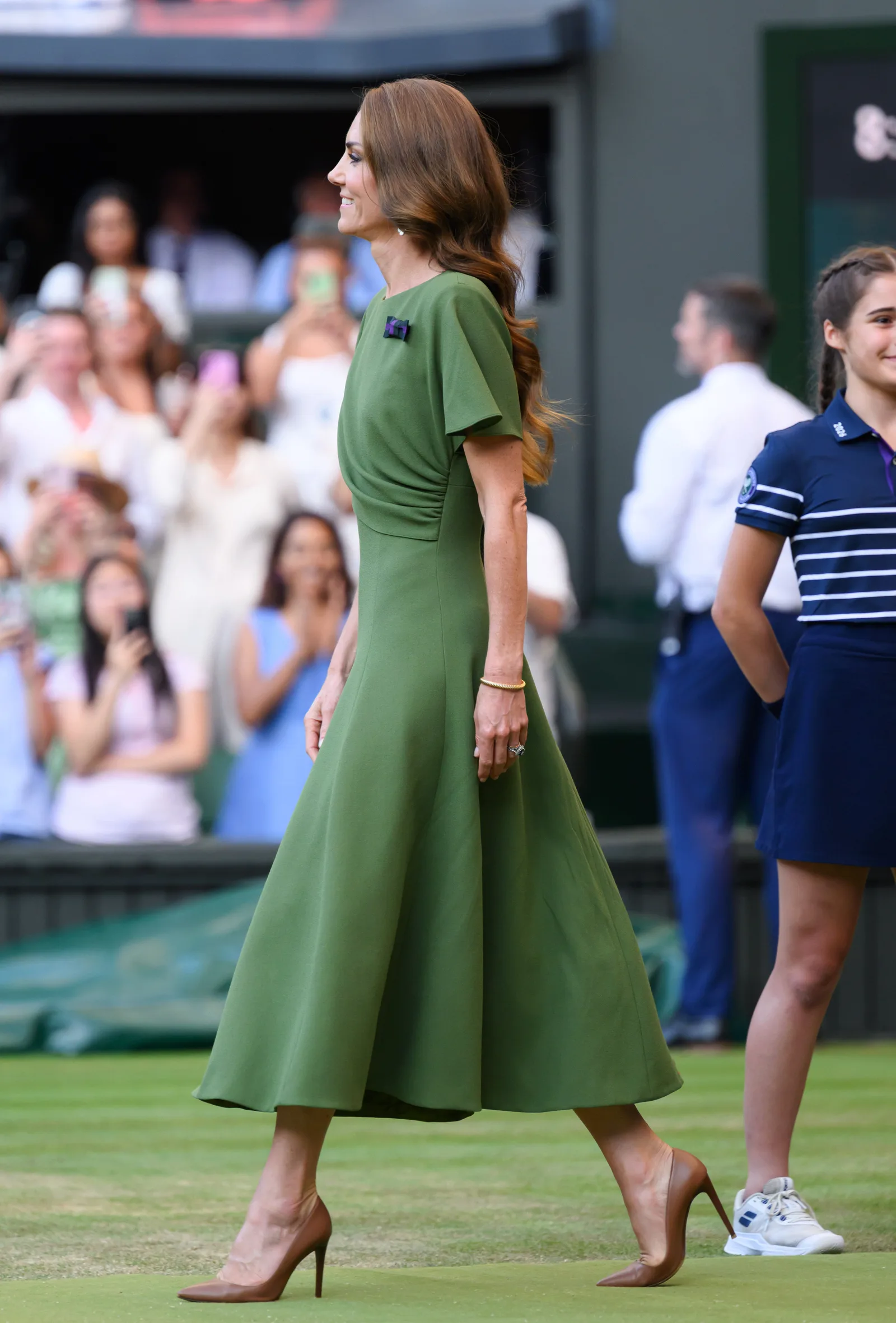 From the side, the dress shows its soft draping and cape-style sleeve, giving the outfit graceful movement as Catherine walked across the court. The olive-green shade complemented the famous Wimbledon setting.