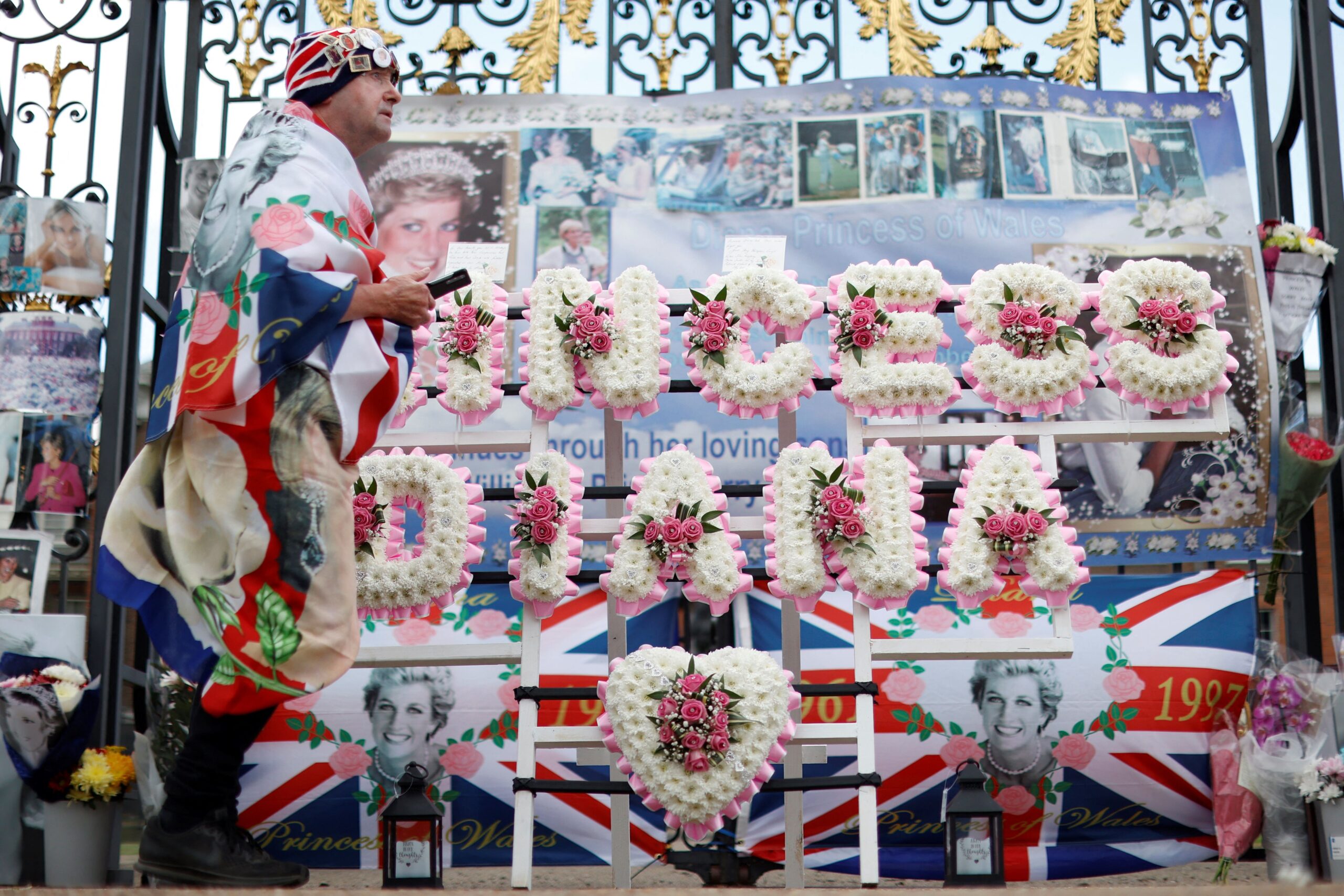 A man wrapped in the British national flag in front of a memorial for Diana, Princess of Wales, in front of Kensington Palace in London, England, on August 31, 2022.