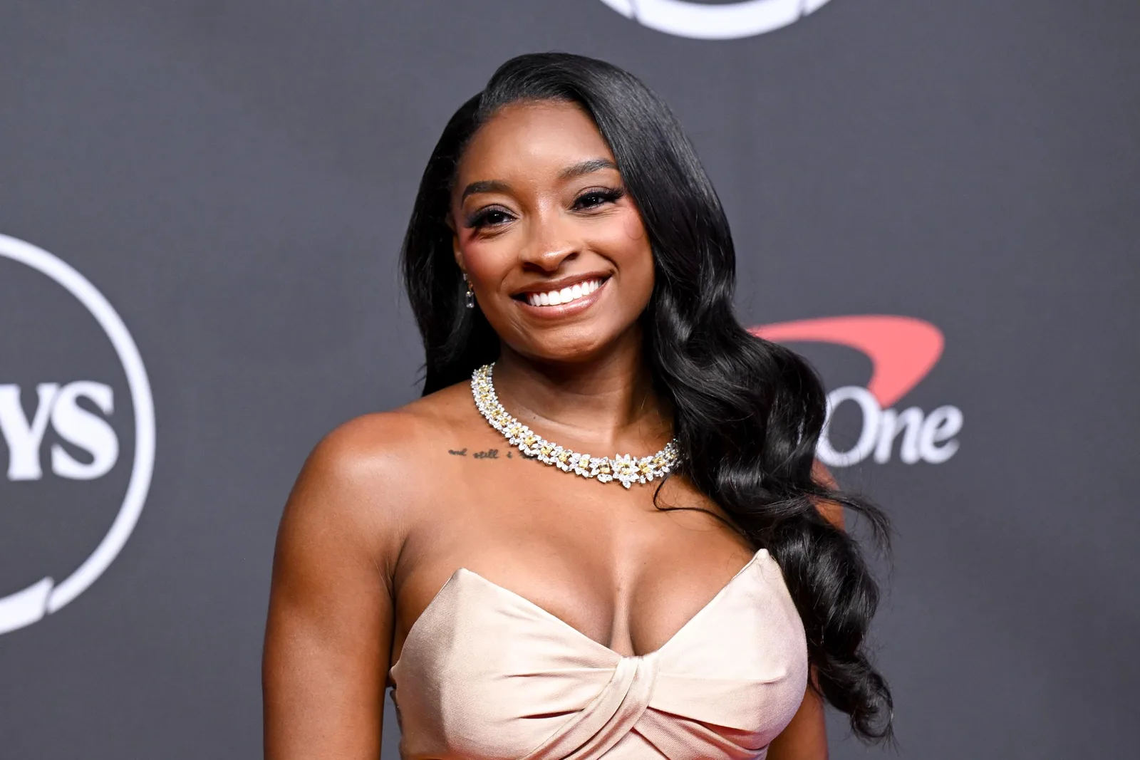 This close-up shows the details that were harder to notice in the viral video. Biles' sparkling necklace, soft waves, and structured bodice became part of the fashion conversation that unfolded alongside the debate over the couple's red carpet moment.