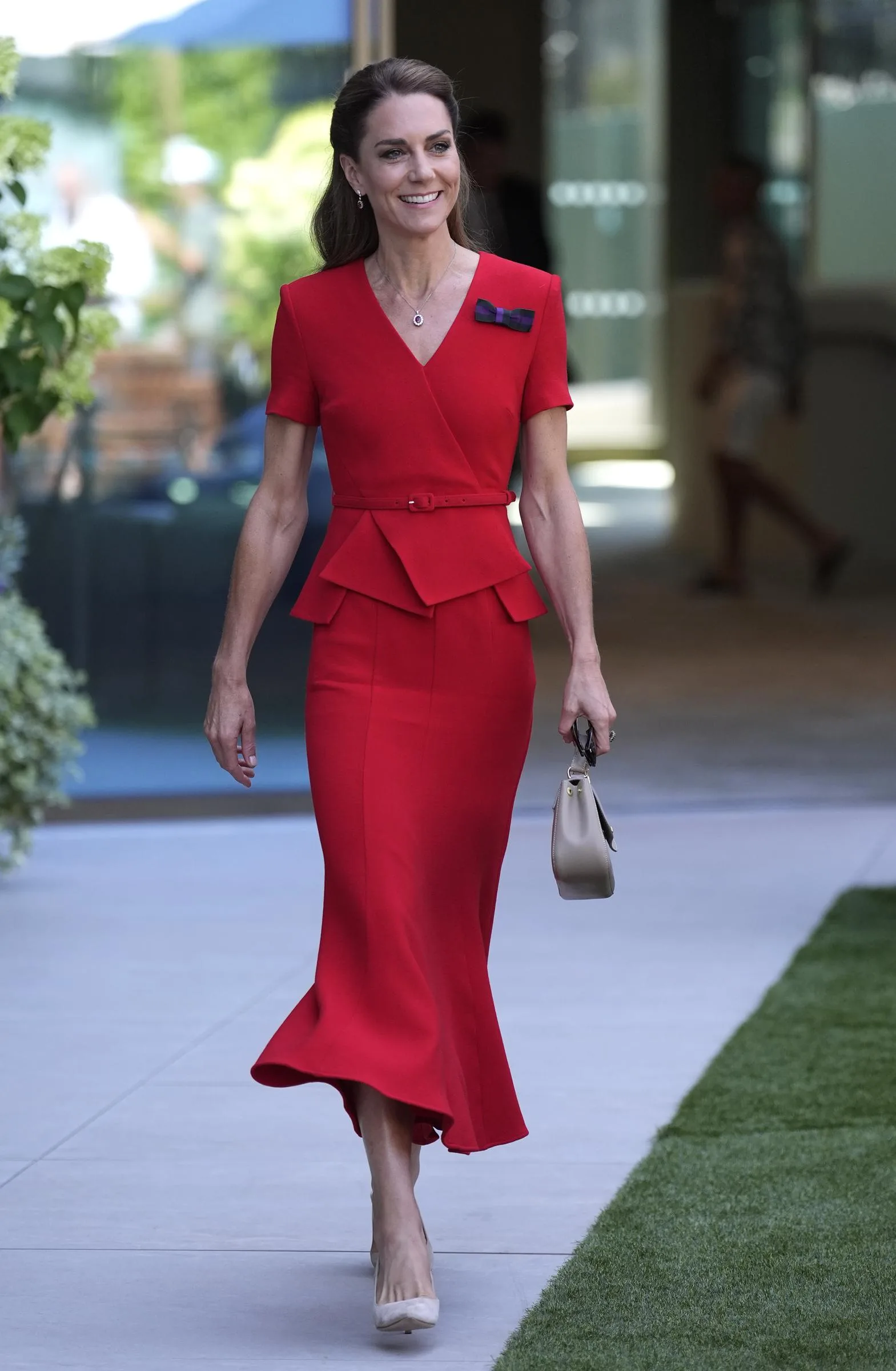 The fitted red dress featured a wrapped bodice, a slim belt, and a peplum waist that created a more structured silhouette than her first Wimbledon look. Nude heels and a neutral handbag kept the focus on the vivid color.