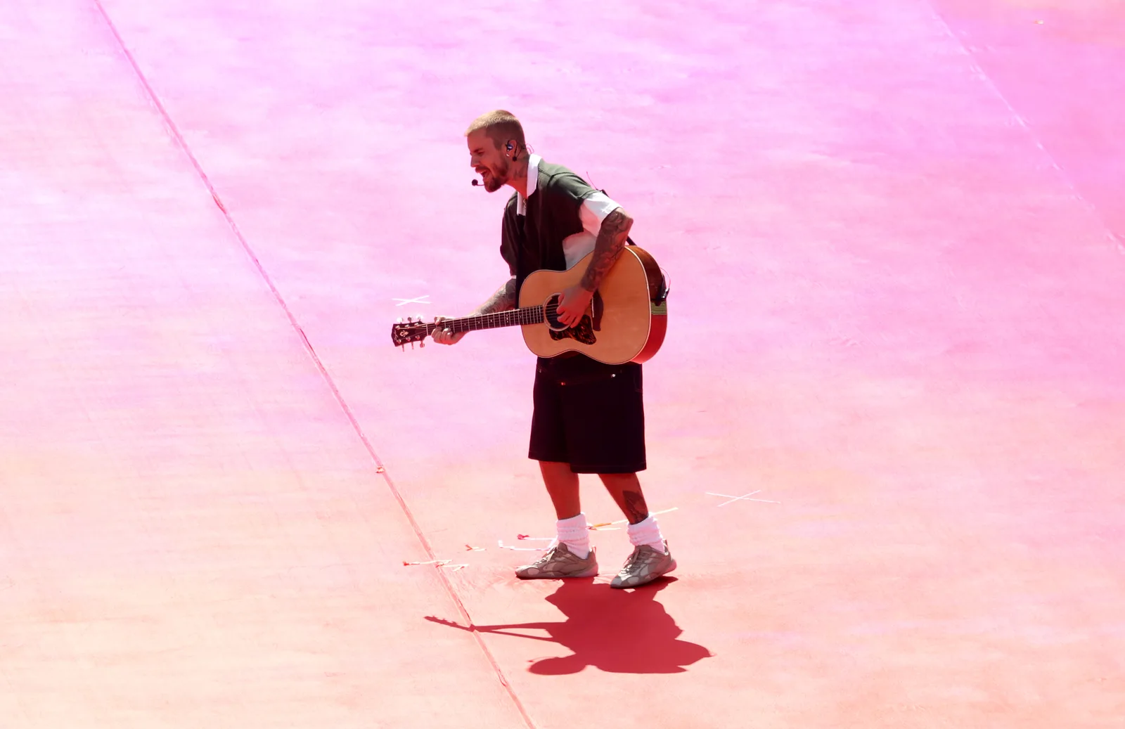 Justin Bieber is captured from a high angle during his Topps Final Halftime Show set, crooning with his guitar against a vibrant, pink-hued stage floor at MetLife Stadium.