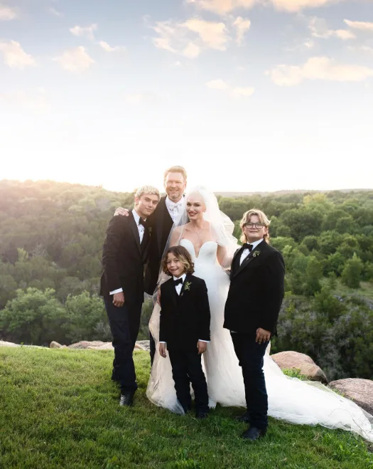 Gwen Stefani and Blake Shelton celebrated their wedding day surrounded by her three sons, Kingston, Zuma, and Apollo Rossdale, all dressed in classic black tuxedos. In this photo, they posed together against a scenic outdoor backdrop on an image shared on July 7, 2021.