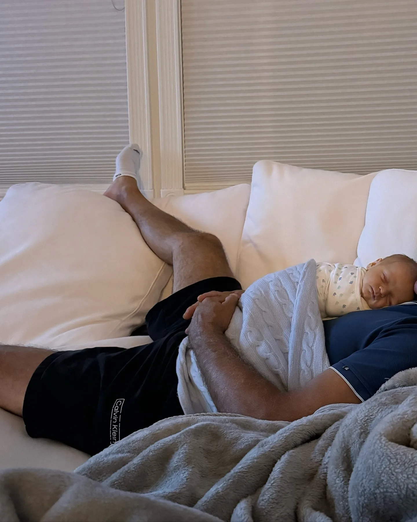 The family's white-furniture theme appears again in this relaxed scene, where a generously sized pale sofa becomes an impromptu resting spot for father and baby. It is another example of how the home's formal architectural bones are softened by everyday family life.