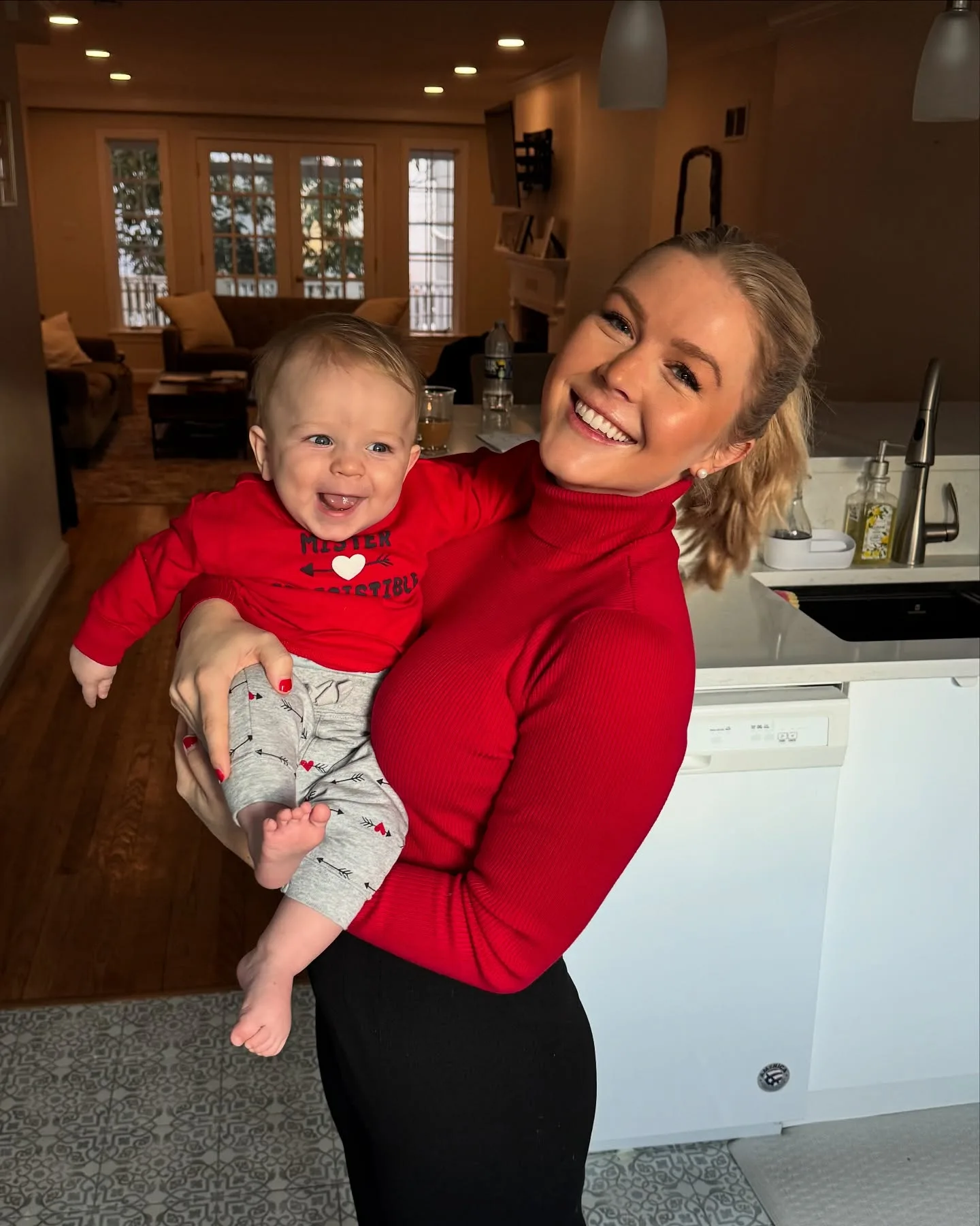 The polished white kitchen also serves as an everyday family space, not merely a glossy backdrop. Leavitt's photo with baby Niko reveals the combination of white cabinetry and darker fixtures that gives the room its crisp, modern contrast.