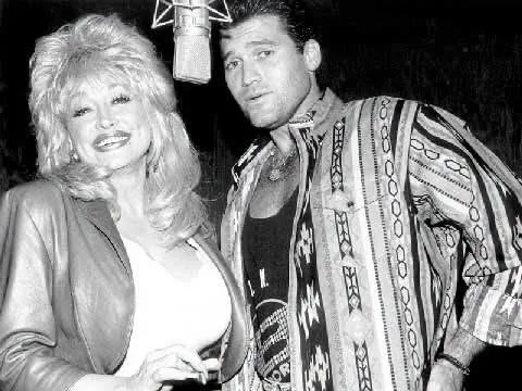 In the studio: Dolly Parton smiles as she shares a microphone with Billy Ray Cyrus during a recording session in this vintage black and white photograph.